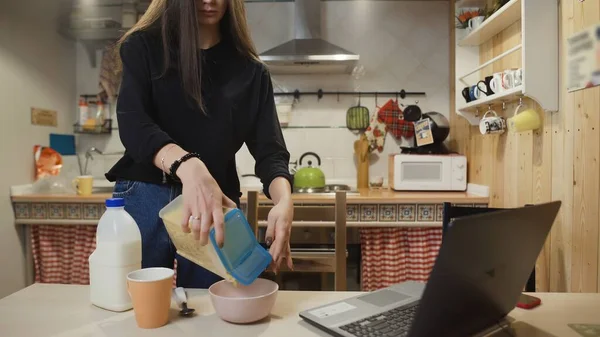 Dizüstü bilgisayarda çalışan ve mısır gevreği yiyen genç bir kadın..