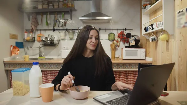 Dizüstü bilgisayarda çalışan ve mısır gevreği yiyen genç bir kadın..