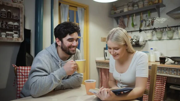 Νεαρό ζευγάρι πίνει τσάι και συζητά για ένα βιβλίο στην κουζίνα — Φωτογραφία Αρχείου