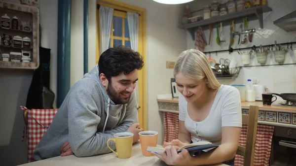 Young couple drinking tea and discuss a book on a kitchen — Stock Photo, Image