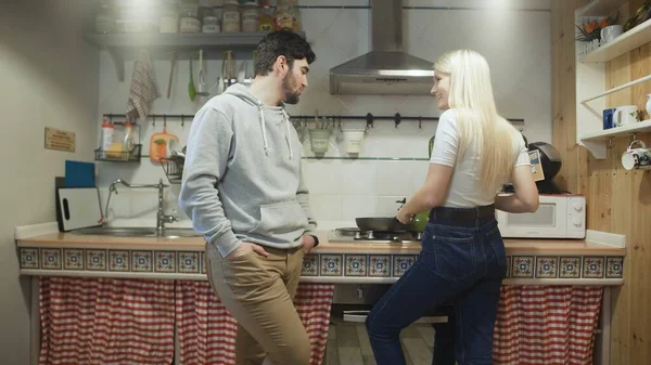 Young wife cooks something on pan and her husband talks to her Stock Image