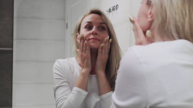 Krem süren ve aynaya bakan kadın doğal güzelliğin ve sağlığın tadını çıkarıyor.