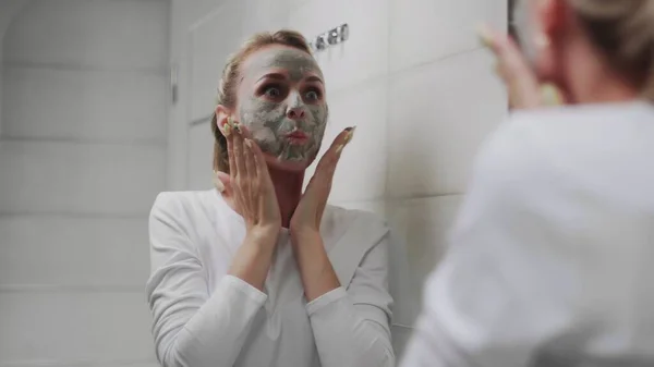 Wanita mengenakan masker tanah liat di wajahnya sambil bercermin — Stok Foto