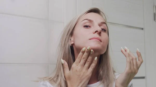 Colóquese de elegante joven mujer mirando a la cámara y tocando su cara en el baño —  Fotos de Stock