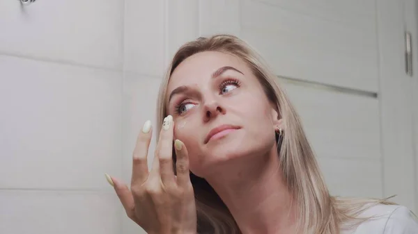 Woman applying cream under the eyes and looking in mirror enjoy natural beauty and healthy — Stock Photo, Image