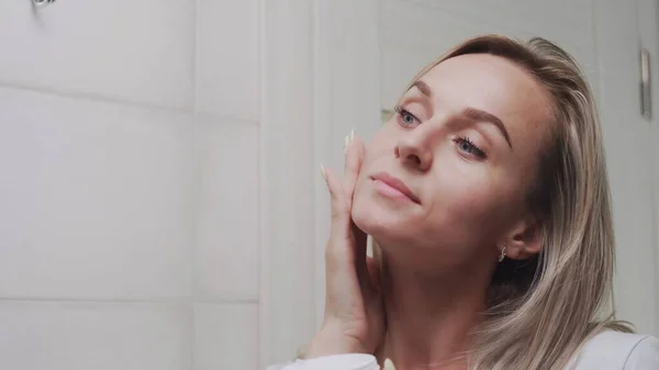 Mujer aplicando crema bajo los ojos y mirando en el espejo disfrutar de la belleza natural y saludable —  Fotos de Stock