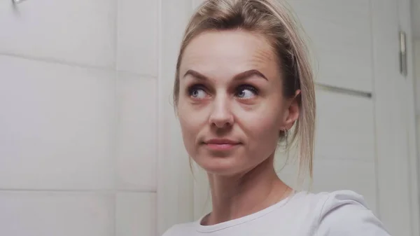 Genç bir kadın saçını elastik bir bandın içine sokuyor ve aynaya bakıyor.