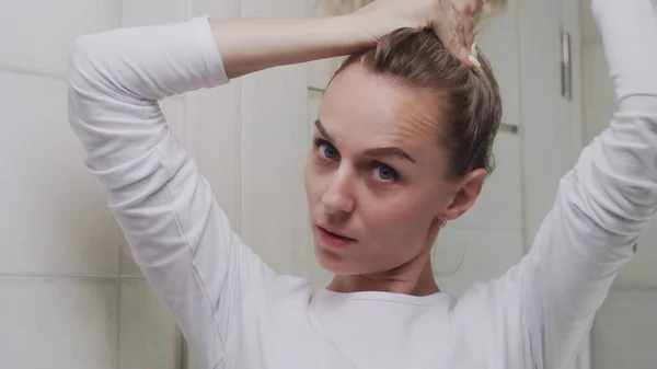 A young woman tucks her hair into an elastic band and look at the camera — Stock Photo, Image