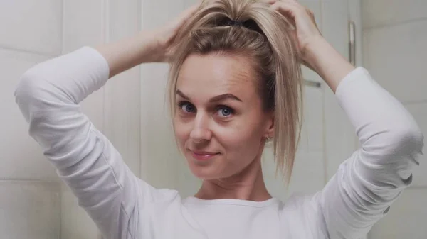 A young woman tucks her hair into an elastic band and look at the camera — Stock Photo, Image