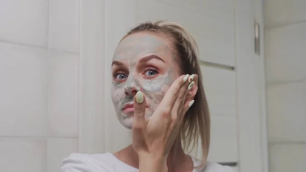 Primo piano della donna che applica la maschera di argilla sul viso guardando la fotocamera — Foto Stock