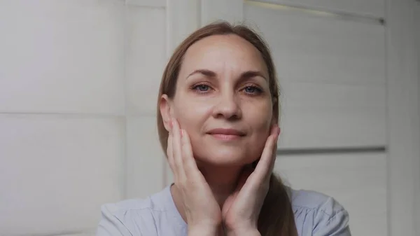 Femme blanche adulte regarde la caméra dans la salle de bain. Lavage du visage, soins de la peau, bien-être — Photo