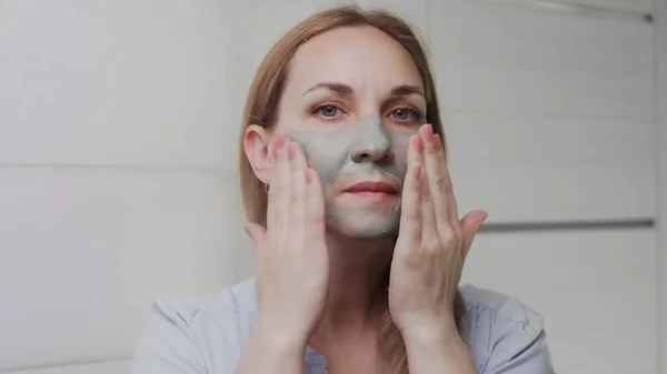Крупним планом Доросла жінка наносить глиняну маску на її обличчя, дивлячись на камеру — стокове фото