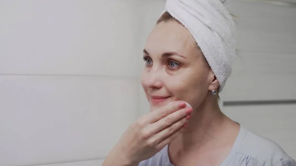 Mujer adulta con una toalla en la cabeza aplicando loción y mirando en el espejo disfrutar de la belleza natural y saludable — Foto de Stock