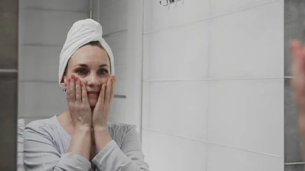 Caucasian woman with a towel on her head in front of a mirror in the bathroom. Face wash, skincare, wellness — Stock Photo, Image