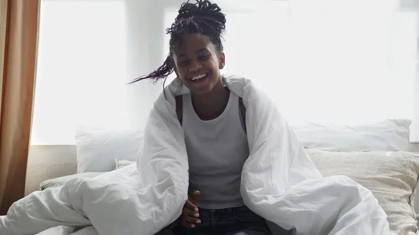 Young happy african woman sits om bed, looks at the camera and smiles — Stock Photo, Image