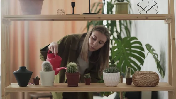 Junge Frau mit roter Gießkanne gießt Zimmerpflanzen in Töpfe — Stockfoto