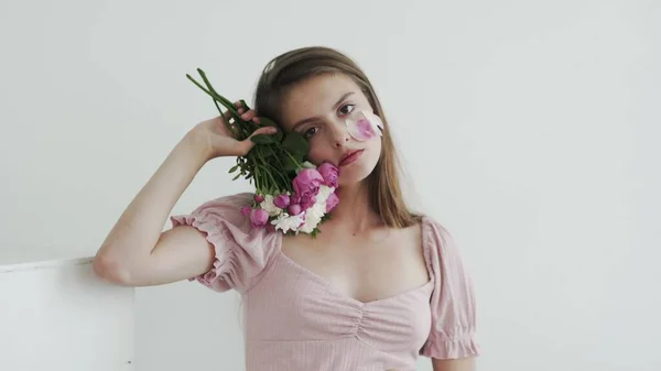 Çekici, güzel, genç bir kadın model. Çiçeklere bakıyor ve kameraya poz veriyor. — Stok fotoğraf