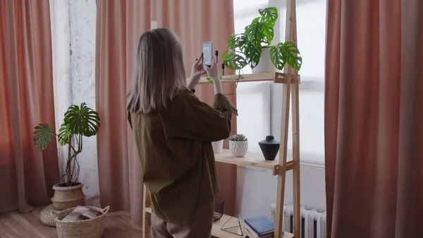 Young woman makes photos of her house plants on shelf — Stock Photo, Image