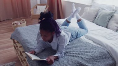 Çekici Afrikalı Amerikalı Kadın yatağa uzanıp kitabı okuyor.