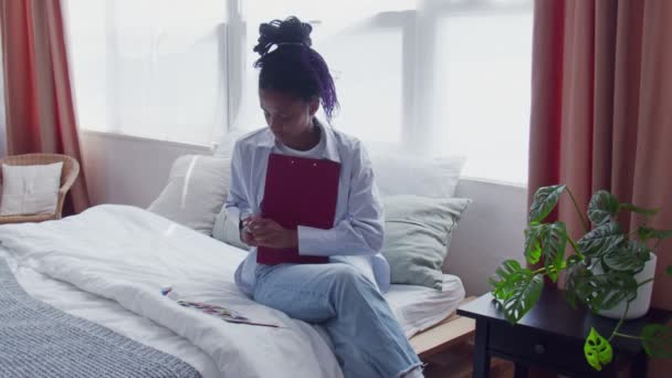 Joven mujer afroamericana sentada en la cama y pintando cuadro — Vídeo de stock