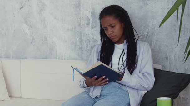 Atraente mulher africana ocupada senta-se na cadeira e faz algumas notas em seu livro de notas — Vídeo de Stock