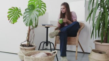 Çekici genç bir kadın telefon sosyal medya platformu kullanıyor ve evde oturuyor. Evde oturuyor. Koltuk keyfi yapıyor.