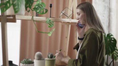 Çekici kadın telefonda konuşuyor ve kaktüsünü kontrol ediyor.