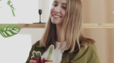 Genç bayan bahçıvan gülümsüyor ve kameraya poz veriyor. En sevdiği kaktüsleri elinde..