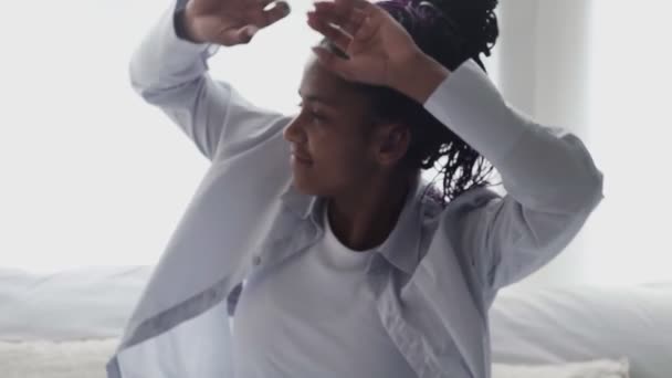 Hezká černoška s kudrnatými vlasy sedící ráno v posteli o víkendu. Unavená mladá Afroameričanka s afro vlasy zívání a protahování paže. — Stock video