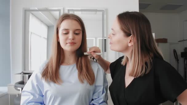 Selbstbewusste kaukasische Maskenbildnerin mit jungem Model blickt im Schönheitsstudio in die Kamera. — Stockvideo