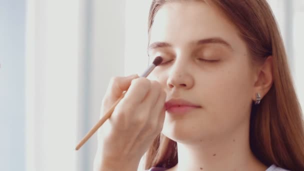 Profesional maquillaje artista haciendo maquillaje para un hermoso modelo caucásico. — Vídeo de stock