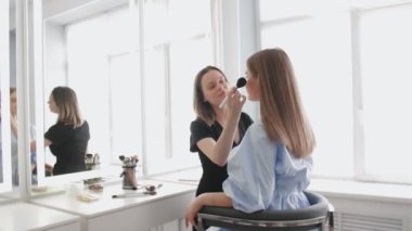 Profesyonel makyöz ve genç model kameraya bakıyor.