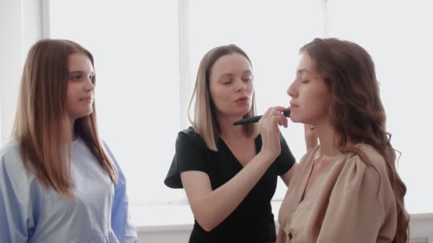 Profesor profesional adulto visagiste entrenar a su joven estudiante para convertirse en artista de maquillaje en la clase magistral en el salón de belleza. — Vídeo de stock