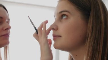 Makyaj sanatçısı kuafördeki kadına göz fırçası çizer. Bir makyözün yakın çekimi