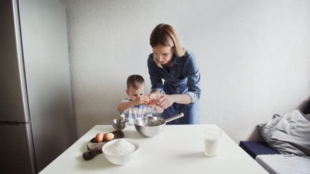 Familjen i ett kök. Vacker mor med liten son bryter ägg i en metallskål — Stockvideo