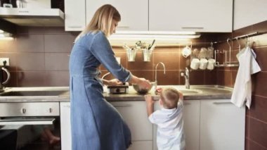 Genç anne waffle makinesinde waffle yaparken oğlu da evde oyuncakla oynuyor.