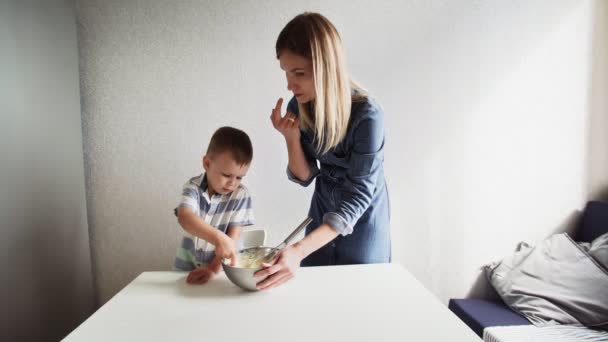 Familie in der Küche. Schöne Mutter mit kleinem Sohn backt Kuchenteig. Sie schmecken den Teig. — Stockvideo