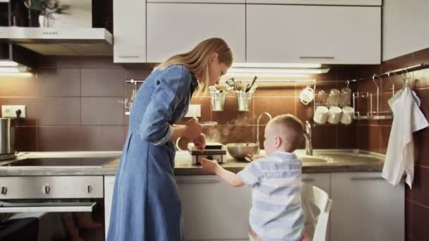 A fiatal anya és a fia várják, hogy a gofrit megfőzzék az otthoni konyhában. — Stock videók