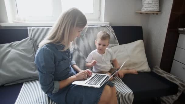 Frau und ihr kleiner Sohn benutzen ein neues Notebook 4K. Junge Mutter arbeitet zu Hause — Stockvideo