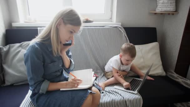 Umtriebige Frau telefoniert und macht sich Notizen, während ihr Sohn mit dem Notizbuch spielt — Stockvideo