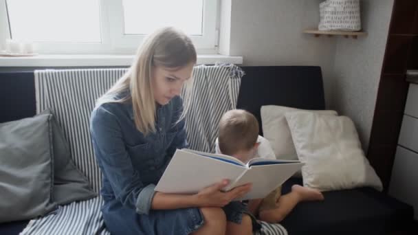 A jovem mãe lê um livro para o filho. Menino se deita no sofá e vai dormir — Vídeo de Stock
