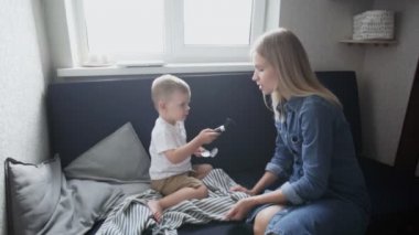 Genç anne ve oğlu evdeki kanepede eğleniyor. Makyaj için büyük fırçayla oynuyorlar.