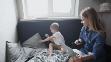 Genç anne ve oğlu evdeki kanepede eğleniyor. Makyaj için büyük fırçayla oynuyorlar.