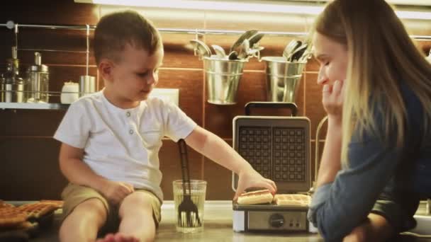 Nahaufnahme einer jungen Mutter und ihres Sohnes backen Waffeln im Waffelbackofen und essen sie in der heimischen Küche — Stockvideo