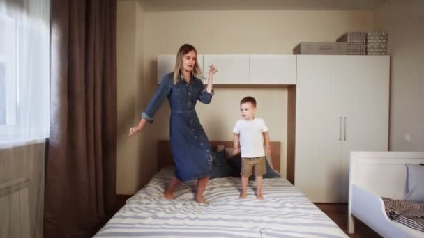 어린 어머니와 행복 한 어린 아들이 침실의 큰 침대 위에서 뛰놀고 있는 모습 — 비디오