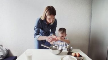 Mutfakta bir aile. Küçük oğlu olan güzel anne, yumurtaları metal bir kaseye kırıyor.