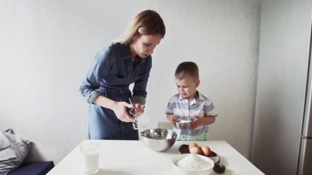 Család a konyhában. Gyönyörű anya kisfiúval. A kisfiú lisztet önt a fémtálba. — Stock videók