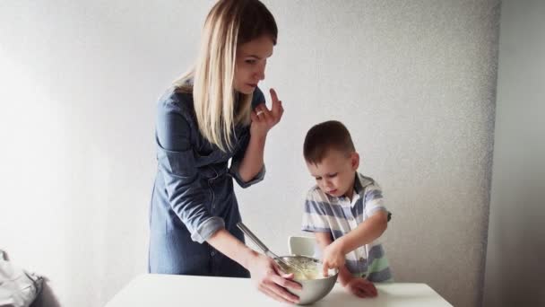 Familie in der Küche. Schöne Mutter mit kleinem Sohn backt Kuchenteig. Sie schmecken den Teig. — Stockvideo