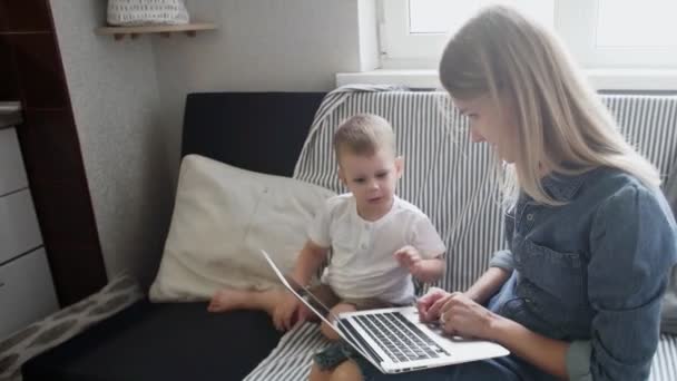 Frau und ihr kleiner Sohn benutzen ein neues Notebook 4K. Junge Mutter arbeitet zu Hause — Stockvideo