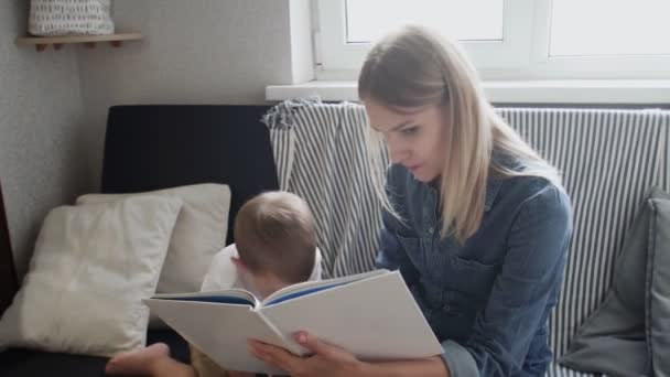 A jovem mãe lê um livro para o filho. Menino se deita no sofá e vai dormir — Vídeo de Stock